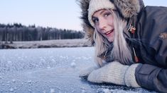 a woman laying on the ice wearing a hat and jacket with her hands in her pockets