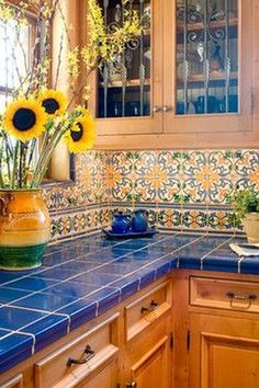 a kitchen with blue counter tops and sunflowers in a vase on the counter