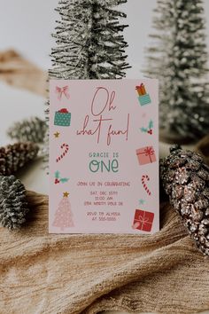 a pink christmas card sitting on top of a table next to pine cones and fir trees