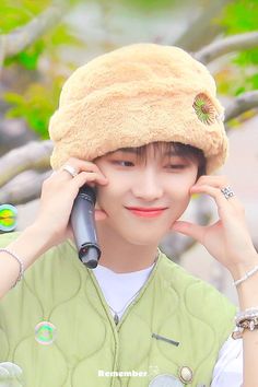 a young man wearing a furry hat while talking on a cell phone in front of a tree