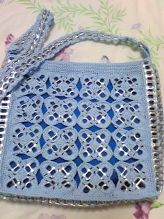 a blue crocheted purse sitting on top of a floral print bed coverlet