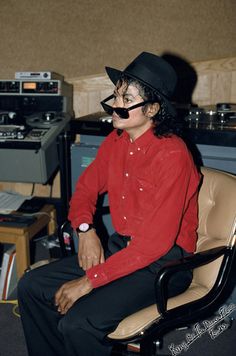 a man in a red shirt and black hat sitting in front of a recording equipment