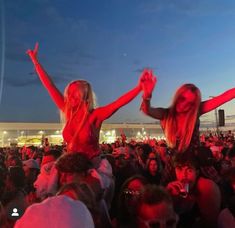 two women are dancing in the middle of a crowd at an outdoor music festival with their arms up