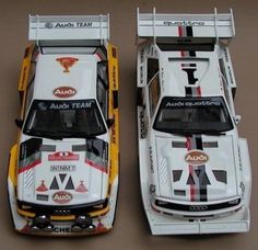 two white and yellow race cars side by side on a brown surface with the words audi team painted on them