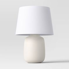 a white lamp sitting on top of a table next to a white light shade over it