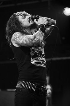 a man with long hair holding a microphone up to his mouth while standing on stage