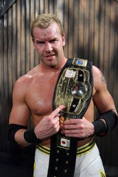 a man holding up a wrestling belt in his right hand and looking at the camera