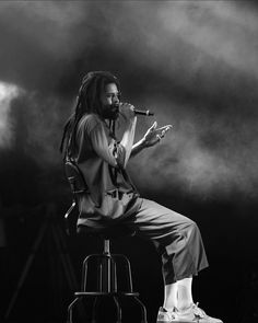 a man with dreadlocks sitting on a chair while holding a microphone in his hand