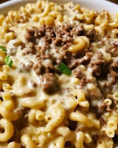 a white plate topped with pasta covered in cheese and ground beef meats, on top of a wooden table