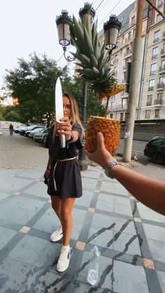 a woman holding up a pineapple in front of a man's hand on the sidewalk