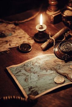 an old world map and some coins on a table with a lit candle in the background