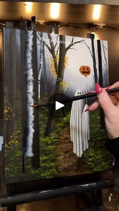 a woman is painting a halloween scene on a canvas