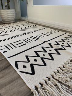 a white and black rug with fringes on the floor next to a potted plant