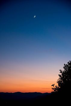 the moon and venus are seen in the sky above trees at sunset, with mountains in the background