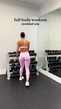 a woman standing in front of a mirror next to a rack of dumbbells