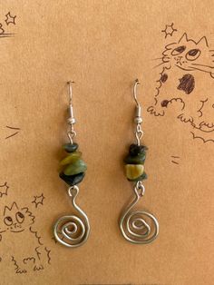 a pair of earrings with green and yellow beads on them sitting on top of a piece of paper