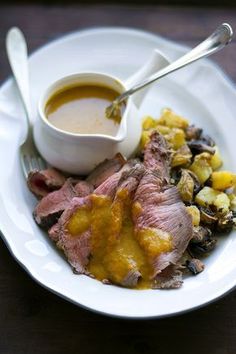 a white plate topped with meat, potatoes and gravy next to a bowl of soup