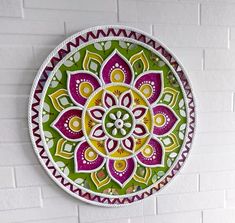 a colorful plate hanging on the wall next to a white brick wall with a green, yellow and purple flower design