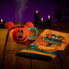 an orange mug sitting on top of a wooden table next to a book and candles