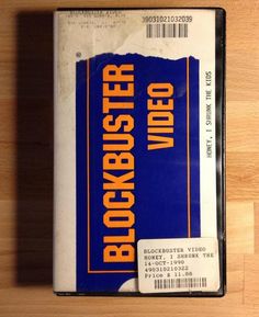 a person holding up a video cassette with the words blockbuster on it in front of a wooden table