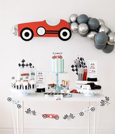 a table topped with cakes and desserts next to silver balloons in the shape of a race car