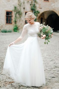 a woman in a white wedding dress holding a bouquet and looking down at the ground