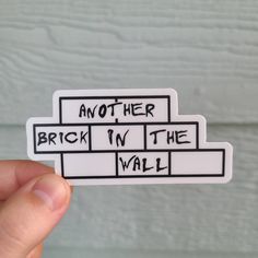 someone is holding up a sticker that says another brick in the wall on it