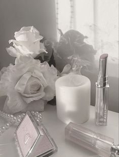 white flowers and cosmetics are sitting on a table next to a mirror, lipstick, and perfume bottle