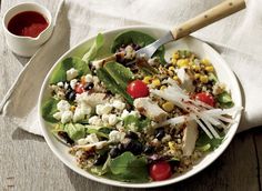 a white plate topped with salad next to a cup of ketchup and a fork