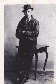 an old black and white photo of a man in a hat sitting on a chair