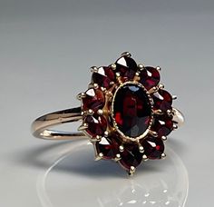 Garnet ring; striking vintage bohemian garnet ring in 10K yellow gold. Gorgeous natural rose cut claret colored garnets set in a halo around a large center rose cut garnet in a pretty flower formation. The ring weighs a sturdy 3 grams. The ring face measures 15 mm N to S x 12 mm E to W. The largest center rose cut garnet measures 6 mm x 5 mm and the smaller round cut "halo" garnets measure 3 mm across. Total garnet carat weight for the ring is estimated 2.10 carats. Currently a size 7 and could Vintage Garnet Engagement Ring, Oval Garnet Ring, Vintage Rings Engagement Antiques, Garnet Engagement Ring Vintage, Vintage Ruby Engagement Ring, Red Wedding Ring, Antique Garnet Ring, Vintage Garnet Ring, Engagement Ring Victorian