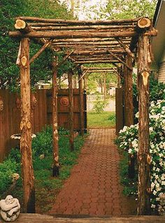 a wooden pergoline with flowers and trees in the backgrouds, next to a brick walkway