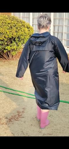 a woman in pink boots and a black raincoat is walking down the street with her back to the camera