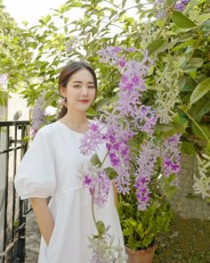 a woman standing next to a bush with purple flowers