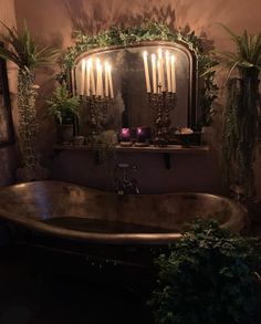 a bath tub sitting next to a mirror with candles on it and plants in the corner