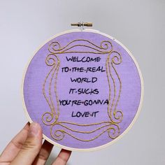 someone is holding up a purple embroidery hoop with the words welcome to the real world, it sucks you'regona love it
