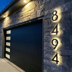 a house with two garage doors and numbers on the side of it that are lit up at night