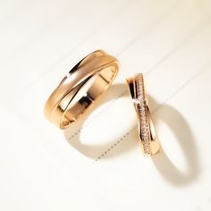 two wedding rings sitting on top of each other next to each other in front of a white background