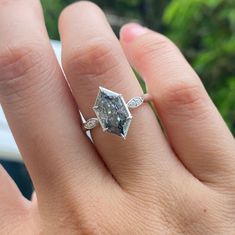 a woman's hand with a diamond ring on top of her finger and leaves around the band