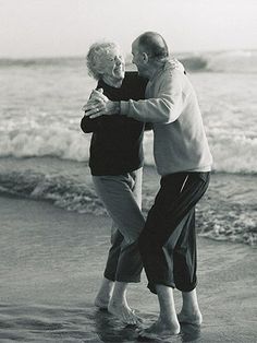 an older couple dancing on the beach in front of the ocean with their arms around each other