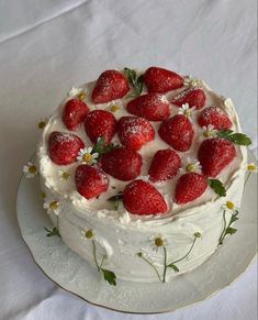 a white cake topped with strawberries and daisies on a tablecloth covered table