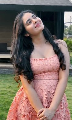 a woman standing in front of a house wearing a pink dress and smiling at the camera