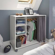 a bedroom with blue walls and a white cabinet filled with clothes on wheels, next to a bed