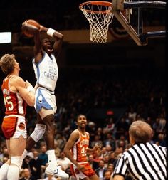 a basketball player jumping up to dunk the ball in front of two other players