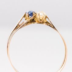 This is part of Chairish’s Fine Jewelry assortment.  Ring in 18 karat rose gold.  Lovely antique charm ring, it is made of a flat double ring like a gold ribbon which asymmetrically retains a natural pearl and a cushion-cut sapphire on its top.  Sapphire weight : approximately 0.14 carat.  Diameter of the pearl : approximately 2.5 / 3 mm.  Height : 7.32 mm, Width : 13.28 mm, Thickness : 3.87 mm approximately, Width at the base of the ring : 3.7 mm.  Total weight of the jewel : approximately 2.2 g.  US Size : 8,5 ;   Authentic antique jewel - French work from the second half of the 19th century.  Our opinion: A pretty antique jewel that has survived the ages without damage.  This item has been used and may have some minor flaws. Before purchasing, please refer to the images for the exact co Sapphire Antique Ring, Black Pearl Ring, Graduation Rings, Ribbon Ring, Edwardian Ring, Vintage Art Deco Rings, Vintage Engagement Rings Sapphire, Gold Sapphire Ring, Charm Ring