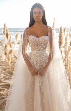 a woman in a wedding dress standing on the beach with her arms behind her back