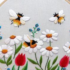 a close up of a embroidery on a white surface with flowers and bees in the middle