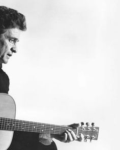 a black and white photo of a man holding an acoustic guitar in his right hand