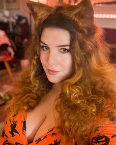 a woman with long red hair wearing an orange shirt and cat ears on her head