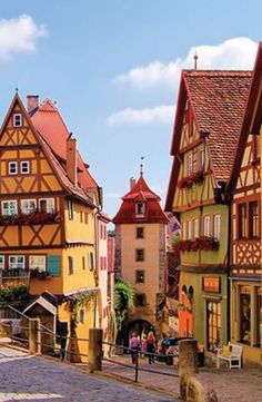 a cobblestone street lined with colorful houses in germany, one has a clock tower on it's side